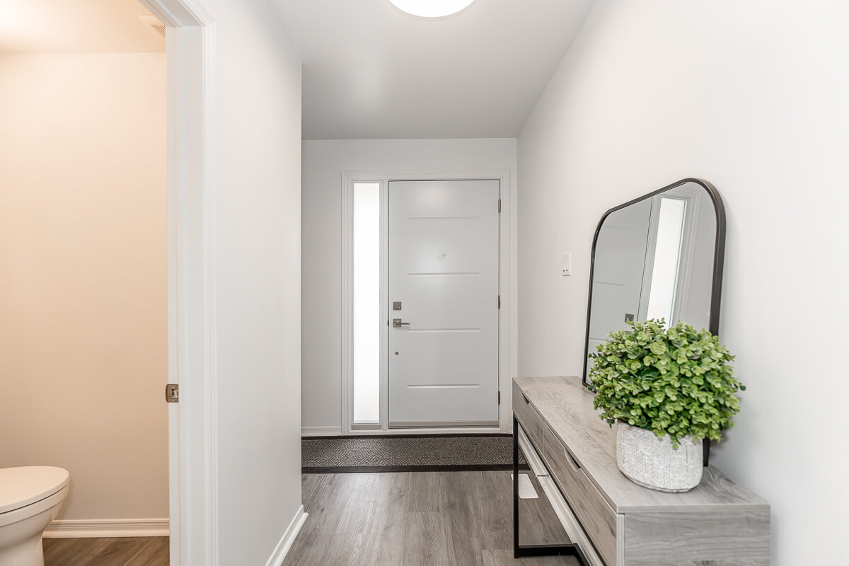 Lifestyle Construction A modern hallway featuring a white front door, a small table with a mirror and potted plant, and a partial view of the bathroom on the left side, showcases the elegance of Toronto Renovation. Home Renovation In The GTA