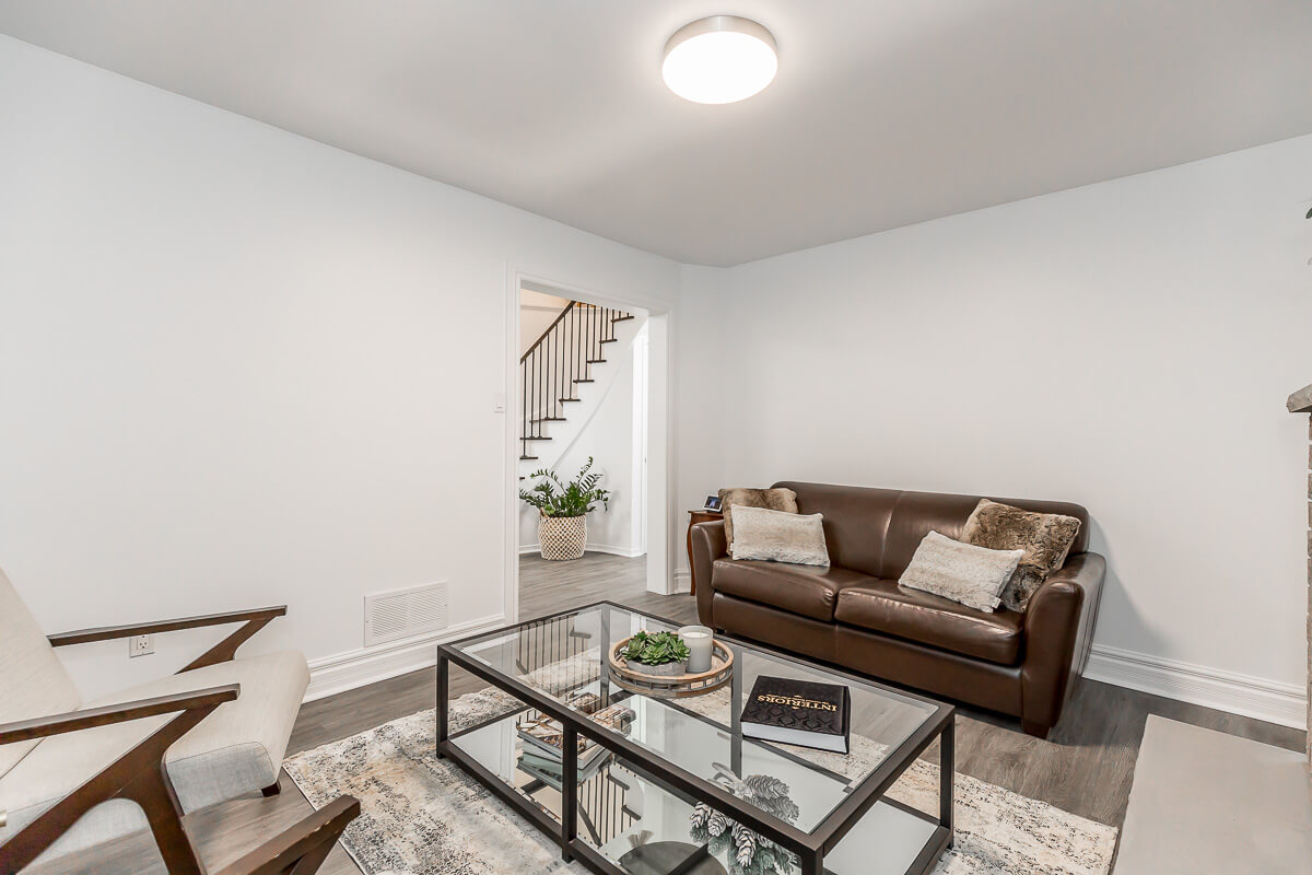 Lifestyle Construction A modern living room with a brown leather sofa, a white armchair, a glass coffee table, and a potted plant near the doorway showcases the stylish results of a Toronto Renovation. Home Renovation In The GTA