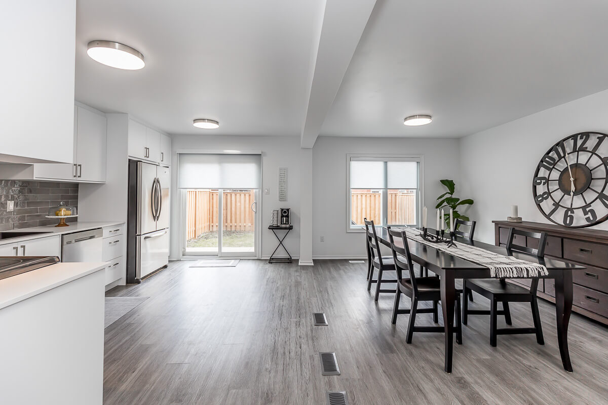 Lifestyle Construction A modern kitchen and dining area with white cabinetry, stainless steel appliances, a large dining table, a wall clock, and large windows with sliding doors leading to a fenced backyard—an exquisite showcase of Lifestyle Construction's craftsmanship in Toronto Renovation. Home Renovation In The GTA