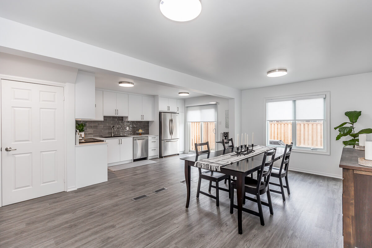 Lifestyle Construction A modern open-concept kitchen and dining area with white cabinets, stainless steel appliances, a black dining table set, and light wood flooring. Natural light enters through a window with a view of a fenced yard, highlighting the craftsmanship of this Toronto Renovation by Lifestyle Construction. Home Renovation In The GTA