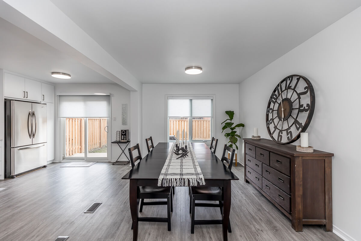 Lifestyle Construction A modern dining room with a dark wood table and six chairs, a large clock on the wall, and a sideboard. This Toronto Renovation creates a space well-lit with natural light from windows and sliding glass doors, perfect for any lifestyle construction enthusiast. Home Renovation In The GTA