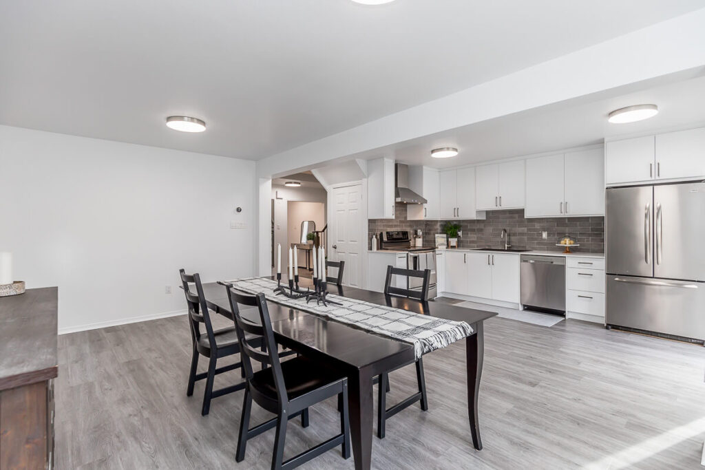 Lifestyle Construction A modern kitchen and dining area with a dark wooden table, black chairs, stainless steel appliances, white cabinets, and gray flooring showcases the pinnacle of Lifestyle Construction in home renovation. Home Renovation In The GTA