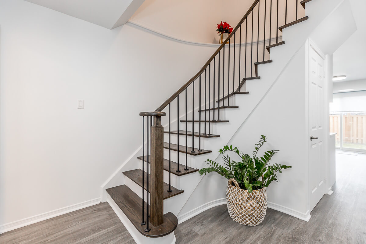 Lifestyle Construction A modern staircase with dark wooden steps and black metal railings showcases the elegance of Toronto Renovation. A red flower decorates the top, while a green plant in a decorative pot sits at the base. The light-colored walls and floor complete this stylish Lifestyle Construction masterpiece. Home Renovation In The GTA