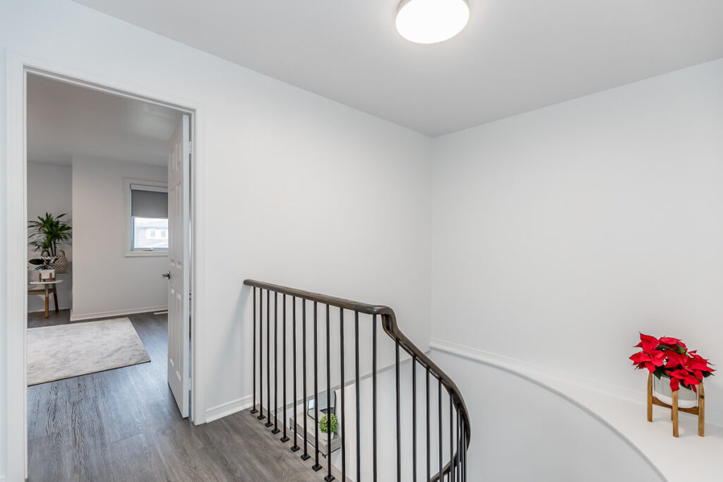 Lifestyle Construction The hallway showcases a curved staircase with a dark wooden railing, a potted plant accentuating its elegance. An open door reveals a room with a desk and chair, epitomizing the exquisite touches of Toronto Renovation. Home Renovation In The GTA