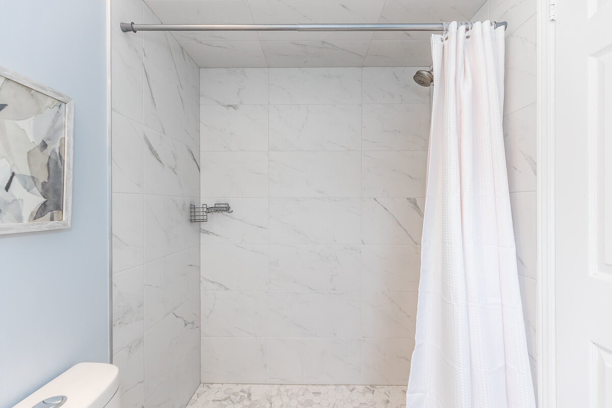 Lifestyle Construction A modern bathroom shower with white marble tiles, a wall-mounted showerhead, and a white shower curtain showcases Toronto Renovation at its finest. Home Renovation In The GTA