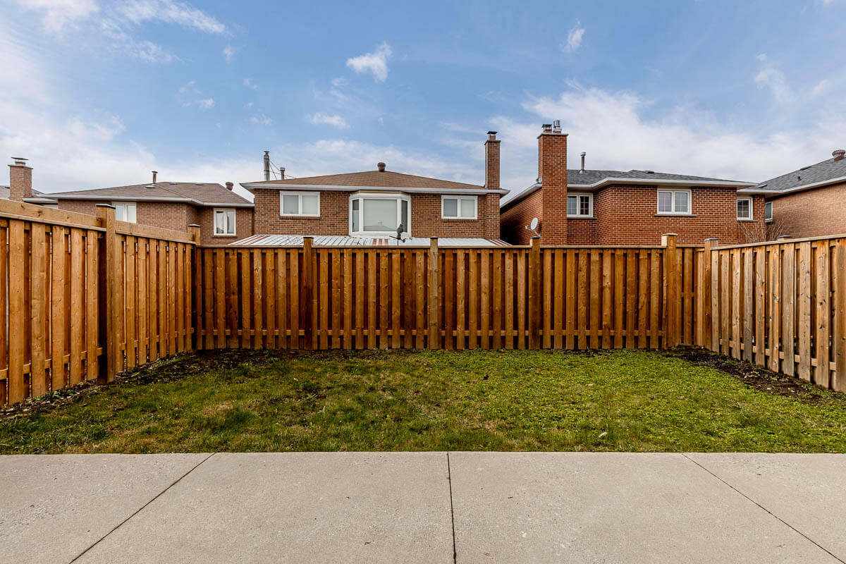 Lifestyle Construction A backyard with a wooden fence enclosing a small grassy area speaks volumes about the tranquil lifestyle construction in this Home Renovation Vaughan project. Two neighboring houses are visible beyond the fence, under a cloudy sky. Home Renovation In The GTA