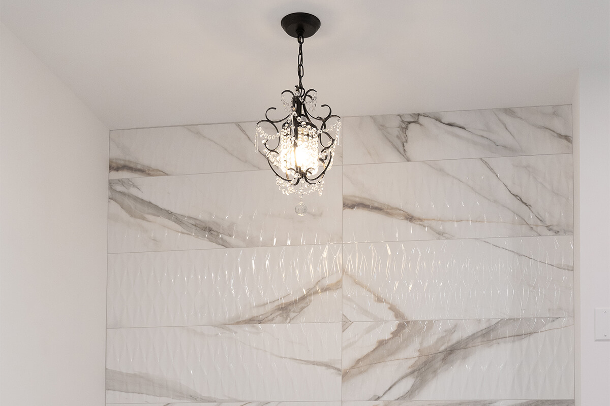 Lifestyle Construction A chandelier with intricate designs hangs from the ceiling, illuminating a wall tiled with large white marble pieces with grey veining—a perfect example of upscale living in Home Renovation Vaughan. Home Renovation In The GTA