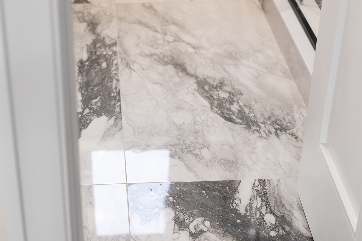 Lifestyle Construction Marble-tiled bathroom floor featuring grey and white hues with a shiny finish, reflecting light from a nearby source, perfect for anyone considering Home Renovation Vaughan. Home Renovation In The GTA