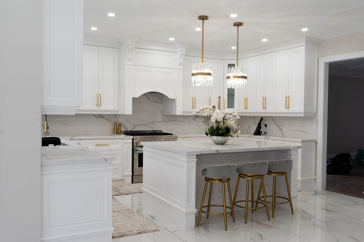 Lifestyle Construction Modern kitchen with white cabinetry, marble countertops, and three gold-accented barstools at an island. Two pendant lights hang above. This Toronto Renovation showcases exquisite design and expert craftsmanship from Lifestyle Construction. Home Renovation In The GTA