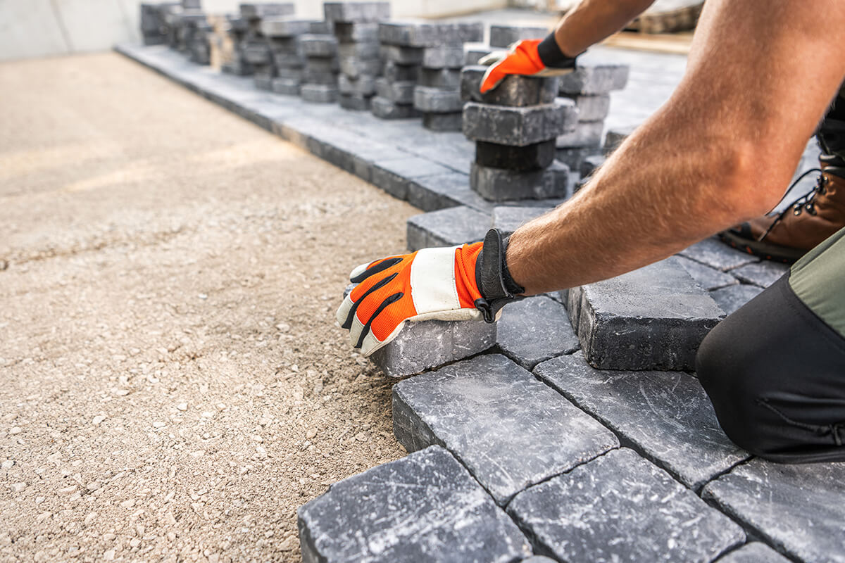 Lifestyle Construction A person wearing gloves is positioning stone pavers on the ground, with stacks of additional pavers nearby, showcasing the meticulous craftsmanship typical of Lifestyle Construction. Home Renovation In The GTA