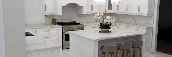 Lifestyle Construction A modern white kitchen with gold accents, featuring marble countertops and backsplash, an island with stools, a gas stove, and pendant lights; expertly crafted by Lifestyle Construction for a flawless Home Renovation Vaughan. Home Renovation In The GTA