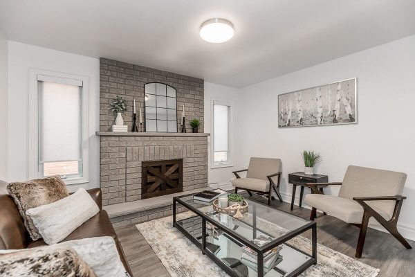 Lifestyle Construction A Toronto renovation showcases a living room with a brick fireplace, two beige chairs, a brown sofa, and a glass coffee table on a patterned rug. A large rectangular mirror and decorative items adorn the fireplace mantel, epitomizing Lifestyle Construction elegance. Home Renovation In The GTA